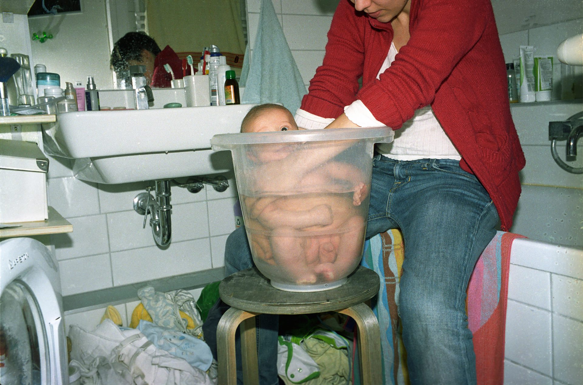 Kobieta kąpie niemowlę w wiaderku.
