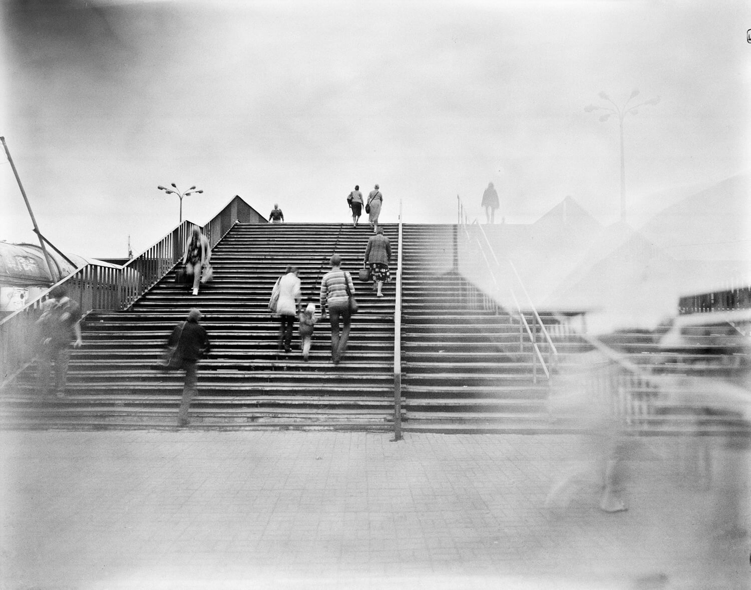 Ludzie chodzący po schodach nad przejazdem kolejowym.